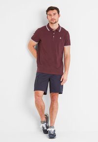 Burgundy polo shirt with white accents, two-button placket. Paired with navy cargo shorts. Model wears navy sneakers.