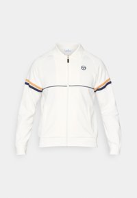 Hvit zip-up jakke i mykt materiale, med krage, brodert logo, og doble horisontale striper i marineblått og oransje på ermene.