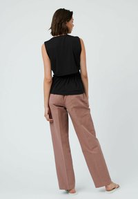 Top senza maniche nero con dettaglio di vita arricciata abbinato a pantaloni a gamba larga rosa chiaro, caratterizzati da una texture liscia e una vestibilità comoda.