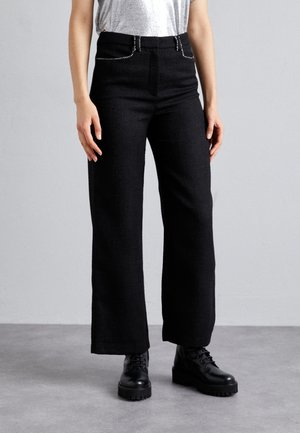 Zwarte wijde broek van gestructureerde stof, voorzien van zilverkleurige hardware accenten en een hoge taille, gecombineerd met zwarte veterschoenen.