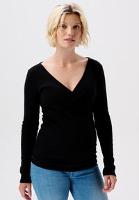 Zwarte, lange mouwen wikkeltop van ribstof, met een diepe V-hals en een aansluitende taille, gecombineerd met lichtblauwe jeans.