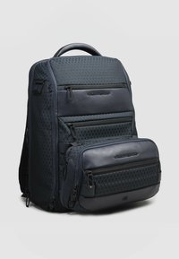 Zaino blu scuro con tessuto a motivo a diamante, molteplici scomparti con cerniera e base in pelle liscia. Dotato di manico superiore per il trasporto.