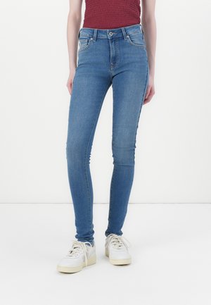 Modré skinny džíny vyrobené z denimu, s vysokým pasem, předními kapsami a hladkou strukturou. Nosené s bílými teniskami.