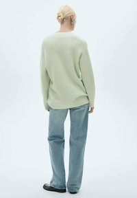 Hellgrüner, locker geschnittener Strickpullover mit rundem Halsausschnitt und langen Ärmeln, kombiniert mit hellblauen Jeans. Flache Schuhe.