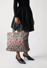 Grande borsa a tracolla marrone con motivi floreali e animali, dotata di un logo "Juicy Couture" rosa, manici doppi e chiusura con zip.