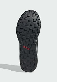 Semelle de chaussure en caoutchouc noir avec des rainures profondes, des motifs texturés et un logo "TRAXION" rouge. Conçue pour l'adhérence et la durabilité.