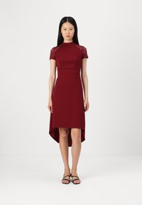 Rochie burgundă cu mâneci scurte din dantelă și tiv asimetric. Țesătură fină cu un corset ajustat și detalii subtile de cusătură. Purtați cu sandale negre plata.
