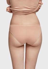 Beige katoenen ondergoed met een gladde textuur, een laaggesneden ontwerp en subtiele geschulpte randen, gepositioneerd op een model van achteren.