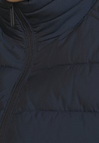 Granatowa kurtka puchowa z wysokim kołnierzem, zamkiem błyskawicznym na całej długości oraz teksturowaną tkaniną z pikowanymi sekcjami dla izolacji.