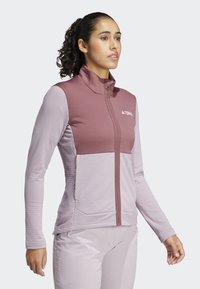 Flis jakna u ružičastoj i svijetloplavoj boji s teksturiranim materijalom na rukavima, stojećim ovratnikom i prednjim zatvaračem. Sadrži logotip na prsima.