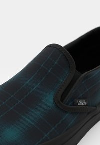 Slip-on obuv ve tmavě modré kostkované barvě s černými akcenty, s elastickými bočními panely a gumovou podrážkou. Viditelná značka loga na boku.