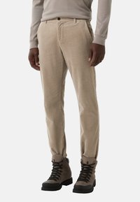 Beżowe spodnie korduroy o prostym kroju, z bocznymi kieszeniami i zapięciem na guzik, w połączeniu z szarymi butami typu high-top.