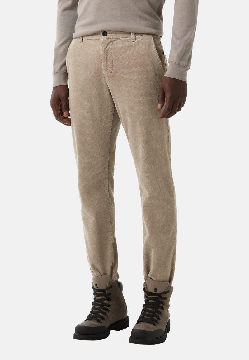 Beżowe spodnie korduroy o prostym kroju, z bocznymi kieszeniami i zapięciem na guzik, w połączeniu z szarymi butami typu high-top.