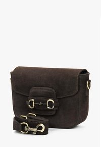 Tmavě hnědá semišová crossbody taška s magnetickým zavíráním klopy, zdobená kovovými detaily a odnímatelným popruhem.