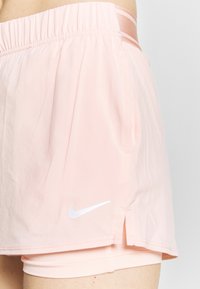 Pantalones cortos de running rosas de Nike con una cinturilla elástica, aberturas laterales y un logo blanco. Hechos de tela ligera con textura suave.