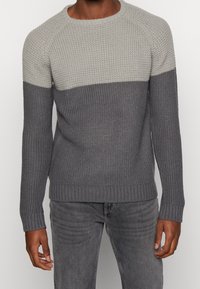 Stickad tröja med en ljusgrå övre del och en mörkgrå nedre del, med rundad halsringning och ribbade ärmslut och nederkant.