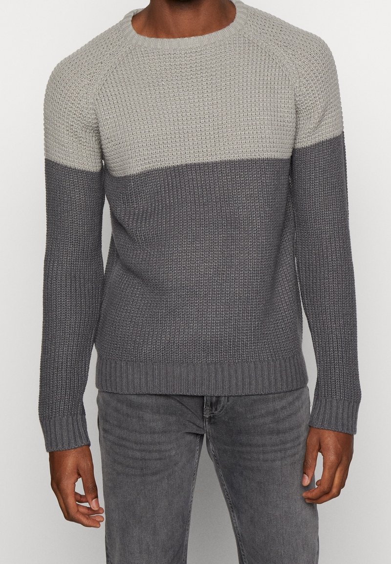 Stickad tröja med en ljusgrå övre del och en mörkgrå nedre del, med rundad halsringning och ribbade ärmslut och nederkant.