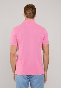 Polo shirt rosa realizzata in morbido tessuto di cotone. Maniche corte, colletto a coste e orlo dritto. Design semplice senza motivi visibili.