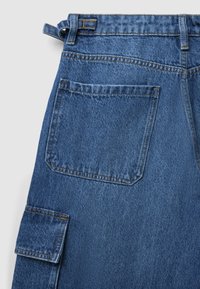 Pantalon en denim bleu moyen avec une finition texturée. Comprend une poche arrière et une poche cargo sur le côté, finition avec des coutures contrastées.