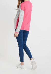 Pitkähihainen paita, jossa on vaaleanpunainen ja harmaa väriestettä, valmistettu pehmeästä kankaasta. Yhdistetty tiukkoihin sinisiin farkkuihin ja valkoisiin tennareihin.