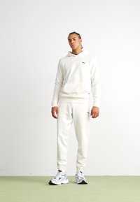 Sudadera blanca y pantalones de tela suave, con un pequeño logo. El conjunto tiene un corte holgado y está combinado con zapatillas deportivas.
