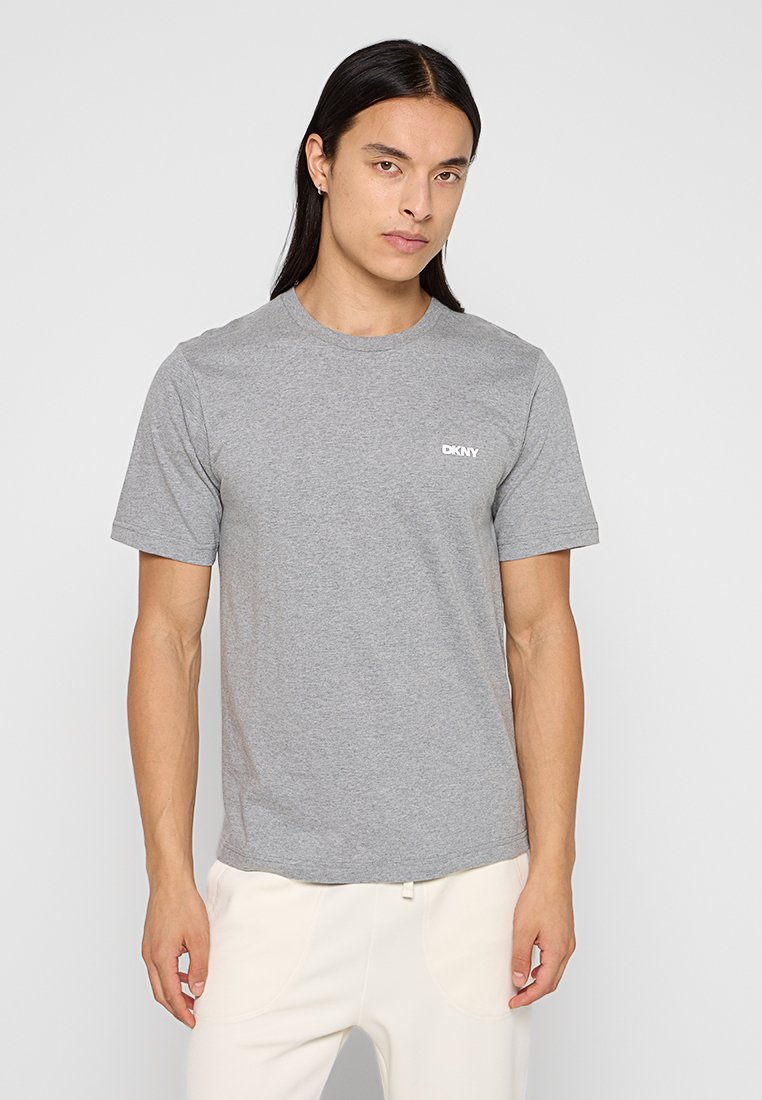 Camiseta de algodón gris con cuello redondo, mangas cortas y un pequeño logo blanco de DKNY en la parte izquierda del pecho. Textura suave.