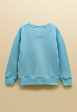 Jasnoniebieska bluza z długim rękawem z prążkowanymi mankietami i ściągaczem, mały haftowany napis "JOULES" blisko dekoltu na beżowym tle.