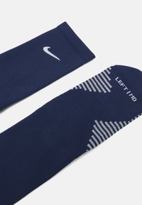Calcetines deportivos de color azul marino, confeccionados con tejido acanalado, que presentan el logo de Nike, un patrón a rayas y el texto "IZQUIERDO" en un lado.