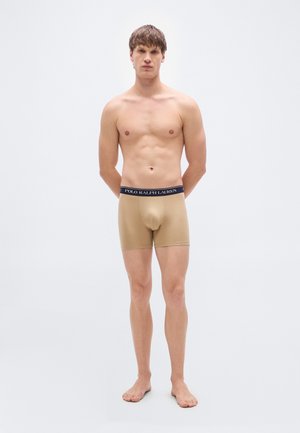 Beige boxershorts voor heren met een marineblauwe tailleband waarop "POLO RALPH LAUREN" staat. De stof is glad en nauwsluitend, reikt tot halverwege de dij.