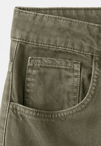 Gros plan sur un tissu en denim vert olive montrant la poche arrière et les coutures détaillées d'un pantalon.