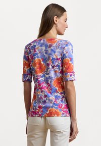 Bloemenprint top met een blauw, oranje en roze patroon, korte opgerolde mouwen en een ronde halslijn. Gemaakt van lichtgewicht stof.
