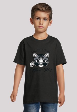 Schwarzes Baumwoll-T-Shirt mit einer weißen Katze, die Sonnenbrillen trägt, und dem Text "DU MUSST MICH VERARSCHEN!" in stilisierter Schrift. Kurze Ärmel.