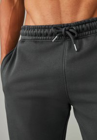 Donkergrijze joggingbroeken met elastische tailleband, trekkoordsluiting en zijzakken. Glad stoftextuur met een slim fit ontwerp.