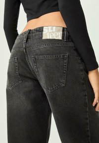 Jeans in denim neri con vita alta, dotati di due tasche posteriori e di un'etichetta sulla cintura. Tessuto testurizzato con una finitura leggermente sbiadita.