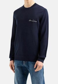 Musta sininen neule tiiviissä muotoilussa, valmistettu pehmeästä materiaalista. Varustettu pitkillä hihoilla ja brodeeratulla "Armani Exchange" -logolla rinnassa.