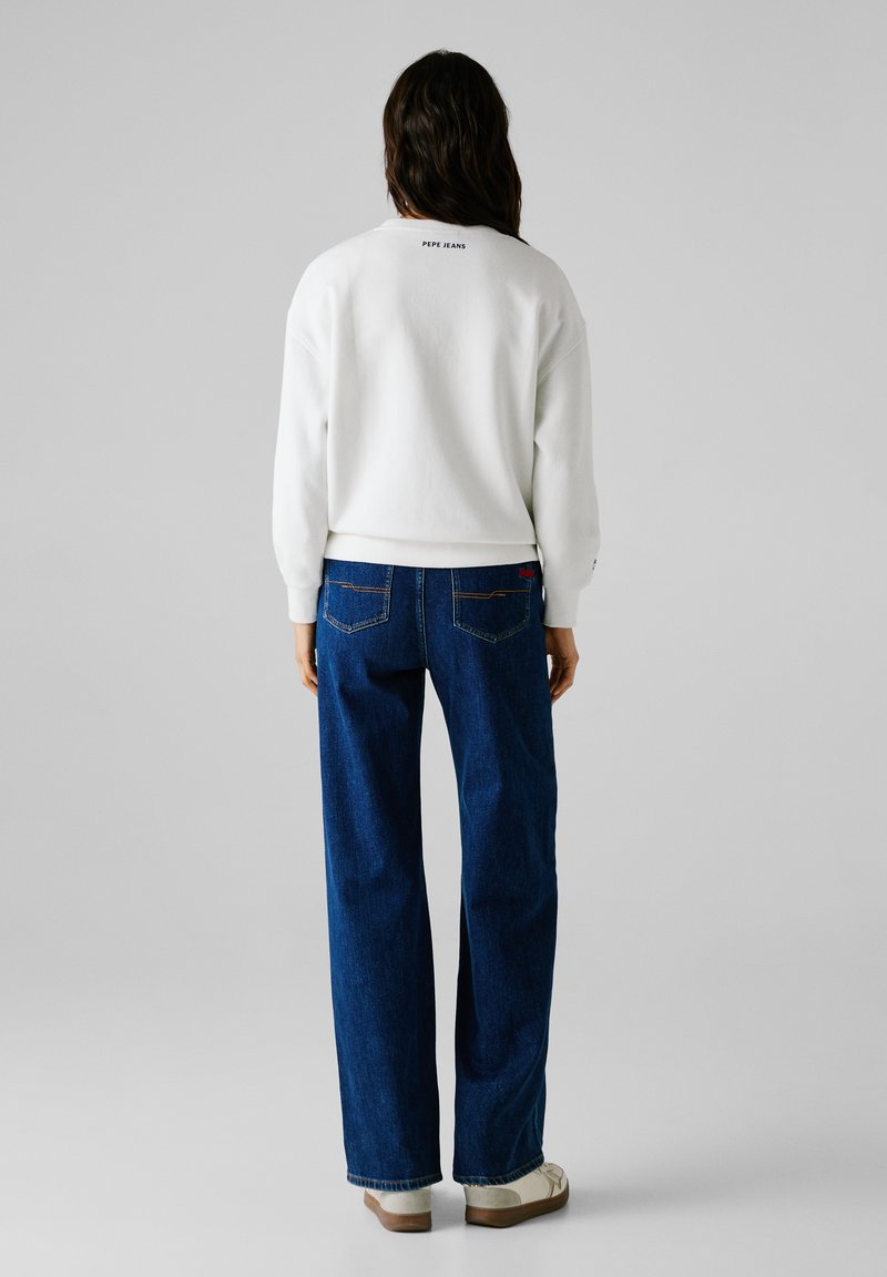 Sudadera blanca con el logo "PEPE JEANS" en la parte trasera, combinada con jeans de pierna ancha azules que cuentan con bolsillos traseros y costuras en contraste.