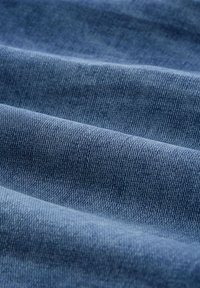 Denim tkanina u srednje plavoj boji s glatkom teksturom, sa suptilnim tvid obrascem. Materijal je lagano naboran i presavijen.