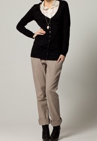 Black button-up cardigan over a light shirt, paired with rolled-up beige pants and high-heeled black boots. Smooth texture and classic design.