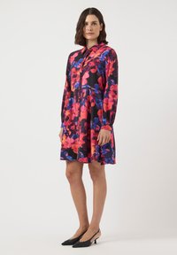 Floral-patterned dress in black, featuring vibrant pink, purple, and blue colors, long sleeves, and a button-down front. Styled with black kitten heels.