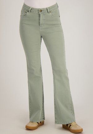 Groene hoge taille wijde broek gedragen door een persoon met beige sneakers, weergegeven van de taille tot de voeten tegen een effen achtergrond.