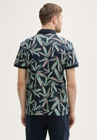 Korte mouwen polo shirt in donker marineblauw met een groen en koraal bladerenpatroon, voorzien van een geribbelde kraag en textuurstof.
