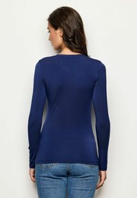 Marineblaue Langarm-T-Shirt mit rundem Ausschnitt, schmalem Schnitt, leichtem Stoff und glatter Textur, kombiniert mit ausgewaschenen blauen Jeans.
