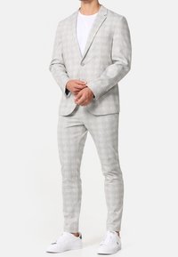 Light grey checkered suit with a tailored fit, single-button blazer, matching pants, and white sneakers. Smooth fabric and minimalistic design.