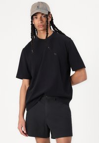 Černé bavlněné tričko s kulatým výstřihem a krátkými rukávy, doplněné černými šortkami. Lehce šedá kšiltovka dokončuje outfit.