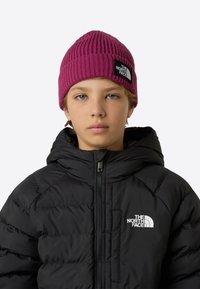 Beanie magenta lavorato a maglia con texture a coste e patch nero con logo. Giacca imbottita nera con zip frontale e tasche laterali.
