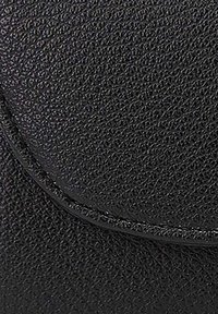 Surface en cuir noir texturé avec un rabat courbé. Le matériau a une finition en relief et un éclat subtil, mettant en valeur des coutures détaillées.
