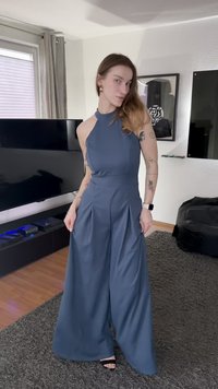 Blauwe jumpsuit met halternek, wijde pijpen, plooien en een getailleerde taille. Gladde stof en minimalistisch ontwerp. Zwarte schoenen maken de outfit compleet.