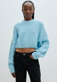 Helles blauer, kurz geschnittener Pullover mit weiten Ärmeln und strukturiertem Strick, kombiniert mit hochtaillierten schwarzen Jeans. Lockerer Schnitt und gerippter Ausschnitt.