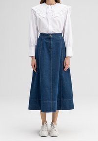 Bílá košile s dlouhým rukávem a velkým volánkovým límcem, v kombinaci s dlouhou modrou denimovou sukní se svisl�ými švy a předním zapínáním na knoflíky.