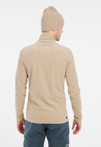 Pullover in pile beige con collo alto, maniche lunghe e finitura testurizzata. Un berretto a coste beige completa il design.